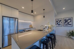 A modern kitchen with a large island, stainless steel appliances, pendant lighting, and a minimalist design.
