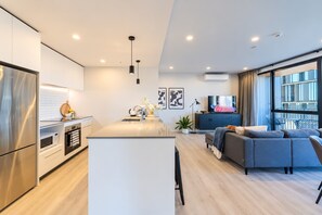 A modern kitchen with a central island, a dining area with a sofa, and a large window offering a view of the city. - Tuam City Side Stay | 2BR + 2BA + Parking (Christchurch)