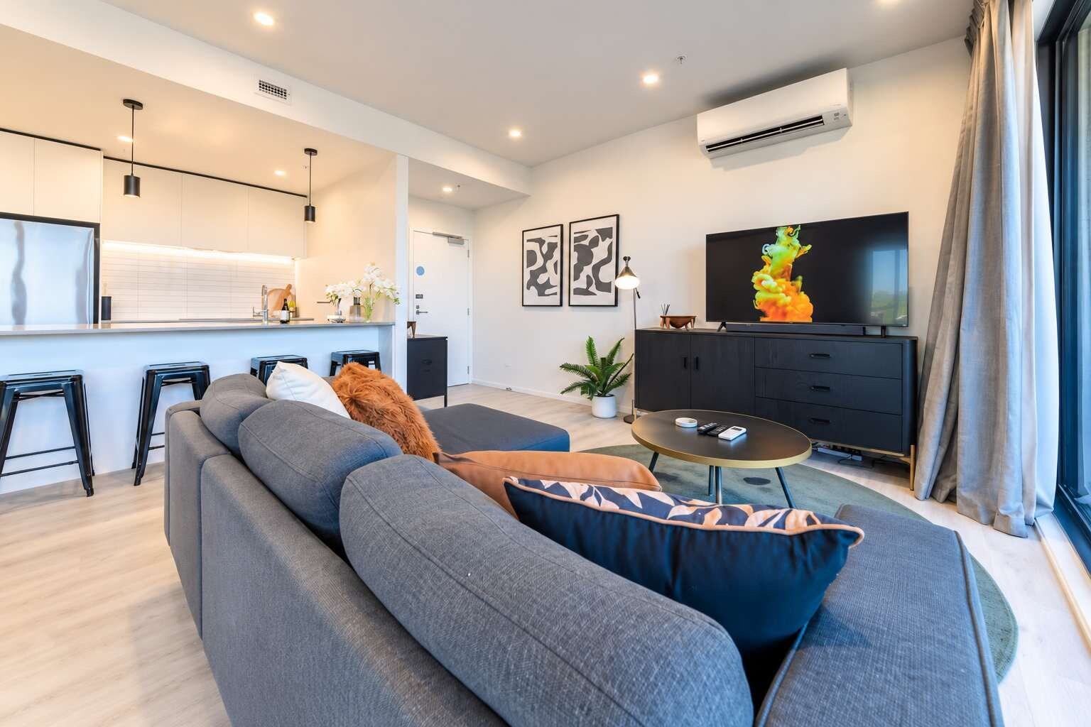 Una sala de estar moderna con sofá, una mesa de centro, televisor y una zona de cocina.
