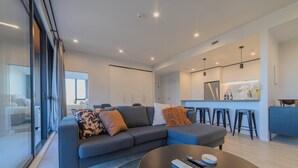 Een moderne woonkamer met een grijze modulaire bank, een ronde salontafel en een keuken met barkrukken.
