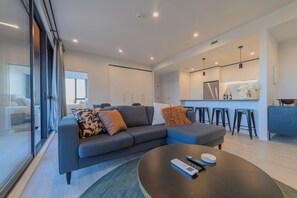 Ein modernes Wohnzimmer mit einem grauen Ecksofa, einem runden Couchtisch und einer Küchenzeile mit Barhocker.