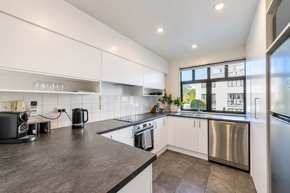A modern kitchen with white cabinets, stainless steel appliances, and a large window providing a view of the outside.