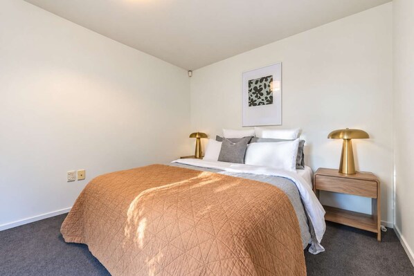 A bedroom with a bed, two bedside tables, a wall-mounted light, and a framed picture.