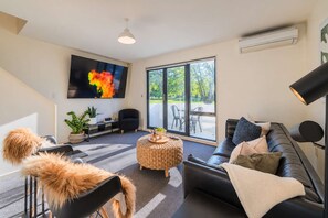 Un salon moderne avec un canapé, un téléviseur, une grande fenêtre et un escalier.