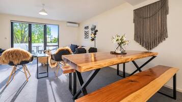 A modern dining area with a wooden table, benches, and a view of the outdoors through large windows.