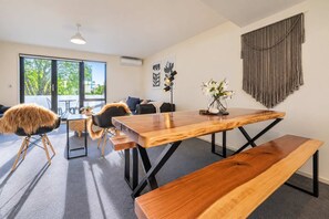 Et moderne spiseområde med et træbord, bænke og udsigt til det fri gennem store vinduer.
