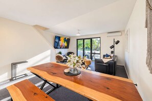 A modern office space with a large wooden table, a sofa, and a TV mounted on the wall.