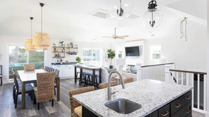 A spacious kitchen with a large island, modern pendant lights, and a dining area with wicker furniture. - New Listing! Pool, Hot Tub & Game Room! (Corolla)