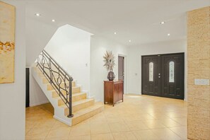 A spacious interior with a staircase, a reception desk, and a dark wooden door.