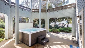 Een overdekt buitengebied met een jacuzzi, betonvloer en een pergola.