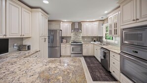 Eine moderne Küche mit weißen Schränken, Edelstahlgeräten, Granit Arbeitsplatten und Einbauleuchten.