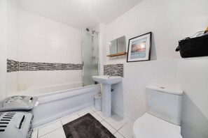 Et badeværelse med badekar, vask, toilet og et billede i ramme på væggen.