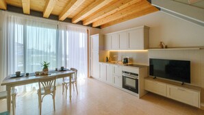 Eine moderne Küche mit Holzbalken, weißen Schränken, einem Essbereich mit Stühlen und einem großen Flachbildfernseher an der Wand.