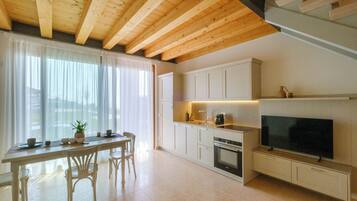 Eine moderne Küche mit Holzbalken, weißen Schränken, einem Essbereich mit Stühlen und einem großen Flachbildfernseher an der Wand.