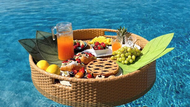 Ein Korbbuschkorb, gefüllt mit Früchten, Gebäck und einem Glas Orangensaft, am Poolrand mit schöner Aussicht.