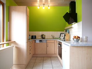 A kitchen with wooden cabinets, a dishwasher, a kettle, and a fruit bowl on the counter.