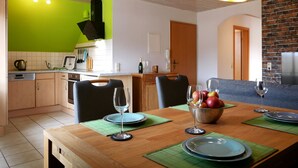 Een eetgedeelte met een houten tafel, stoelen en een schaal fruit.