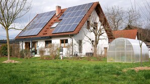 Een huis met zonnepanelen, een kas en een gazon.