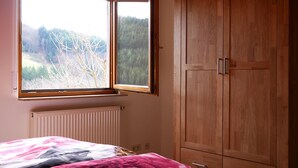 Een slaapkamer met een bed, een raam met uitzicht op bomen en een houten garderobe.