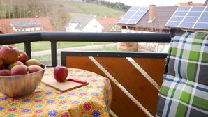 Een balkon met een tafel, een schaal appels en een huis met zonnepanelen op de achtergrond.