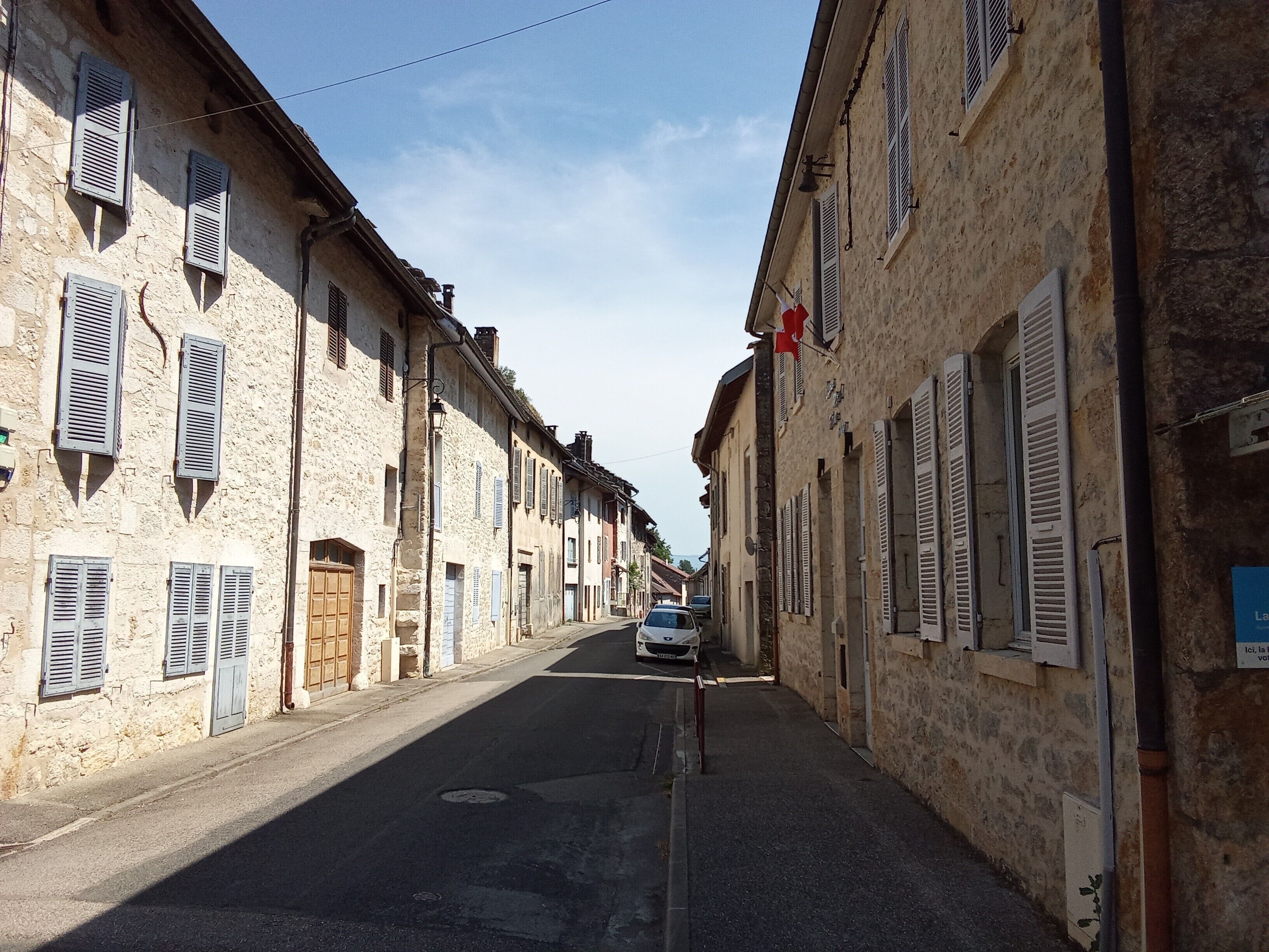 A narrow street lined with stone buildings, some with shutters, and a car parked in the distance.