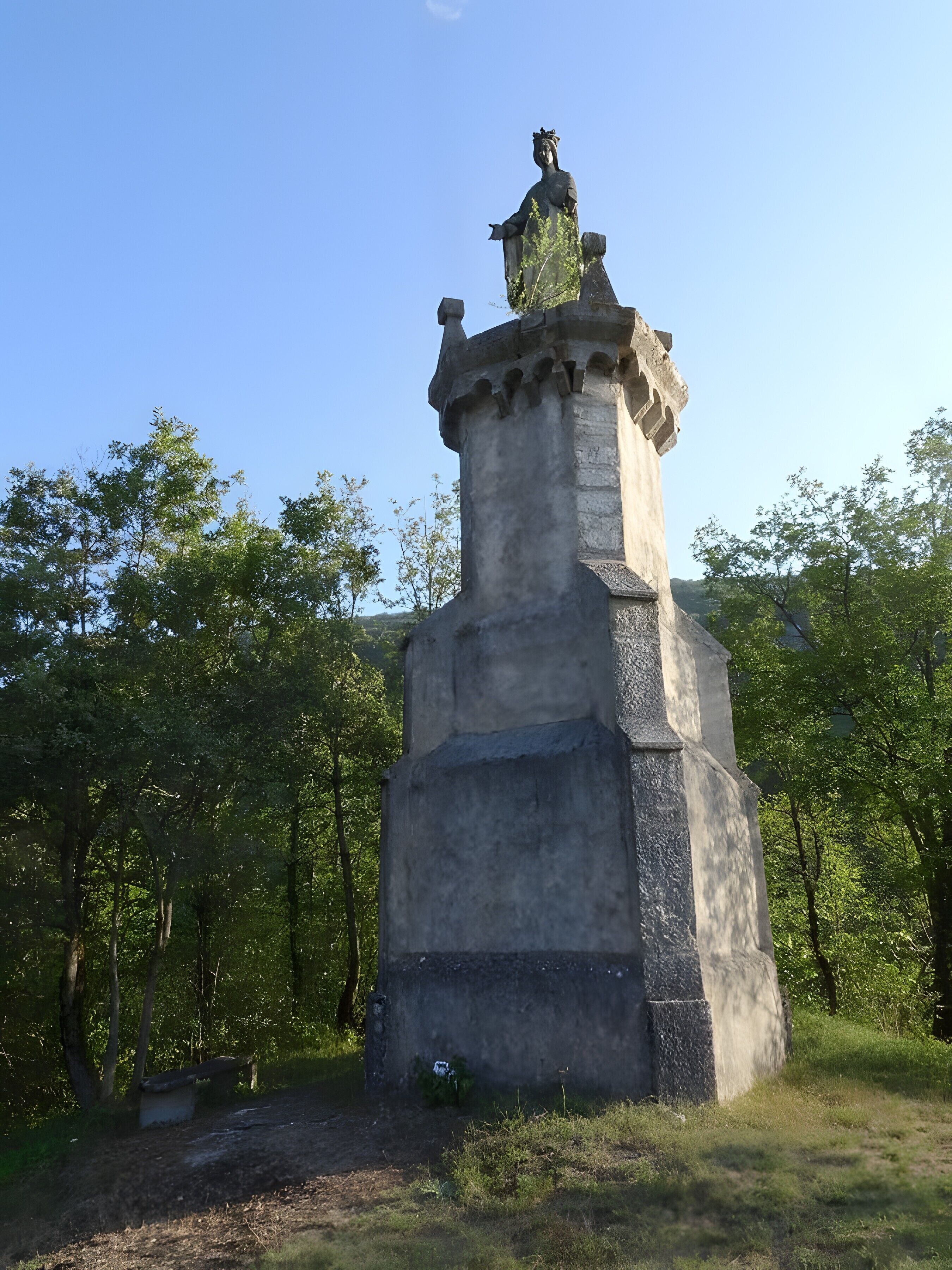 Een stenen monument met een standbeeld erop, omgeven door bomen.