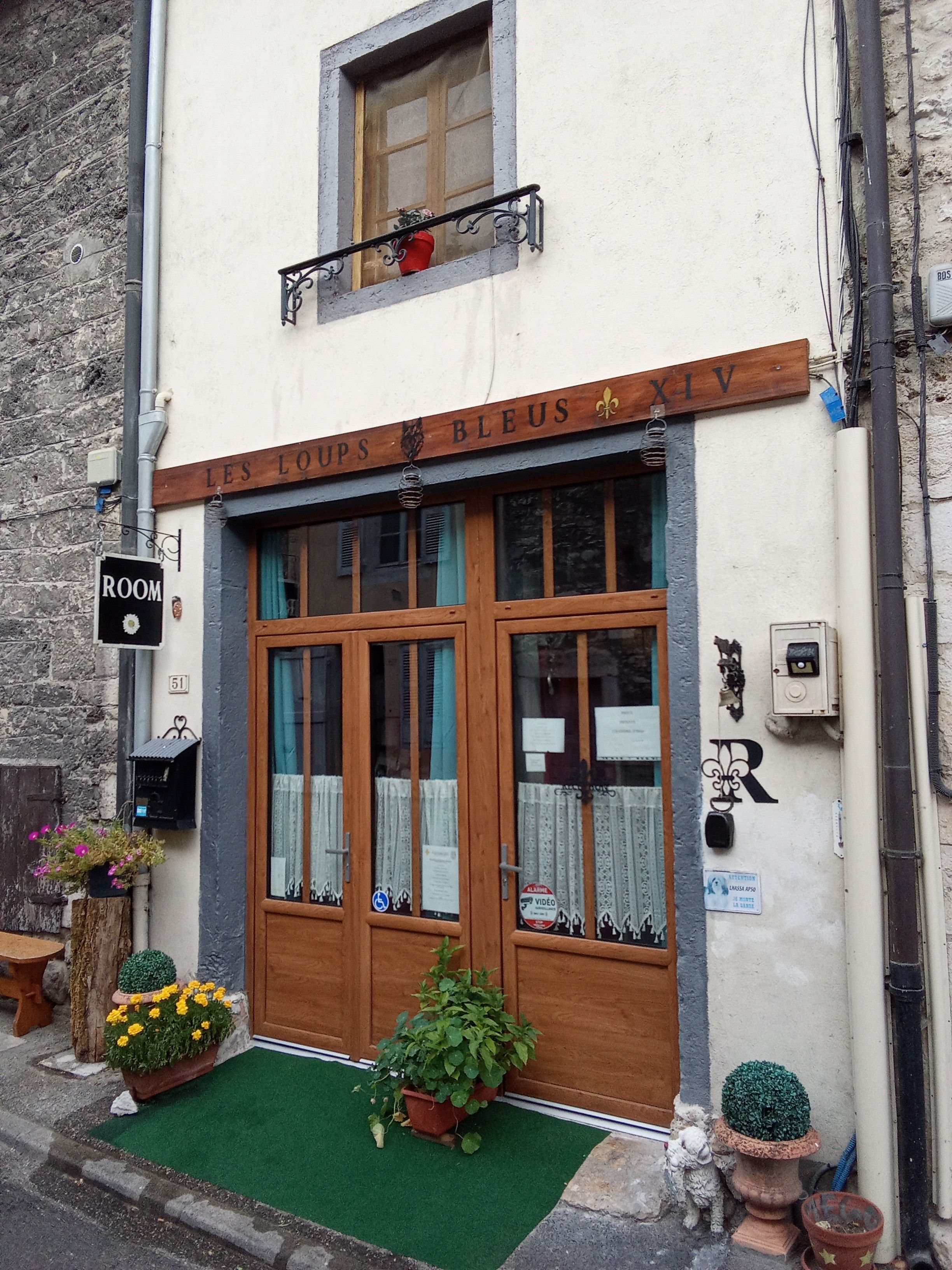 Un bâtiment avec une porte en bois, une enseigne au-dessus de la porte et une petite fenêtre avec un rideau.