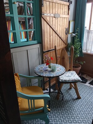 Een gezellige kamer met een groene bank, een klein rond tafeltje met een bloevas, een houten stoel en een vloer met patroon.