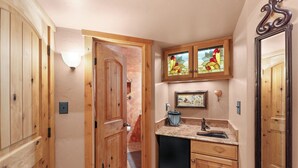 A narrow hallway with wooden doors, a small kitchen area with a sink and countertop, and a stained glass window above the sink.