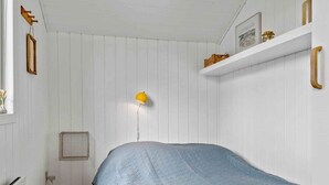Ett sovrum med en enkelsäng, en gul vägglampa och en vit hylla med dekorativa föremål.