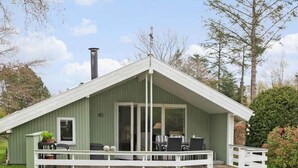 En grön byggnad med en täckt uteplats, en skorsten och en terrass med utemöbler.