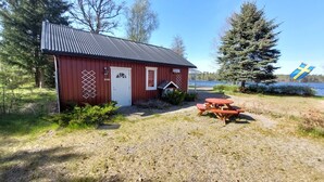 A red wooden cabin with a metal roof, a white door, and a small porch. There is a picnic table in front of the cabin. - Vacation home directly on the Lagan near Markaryd (Markaryd)