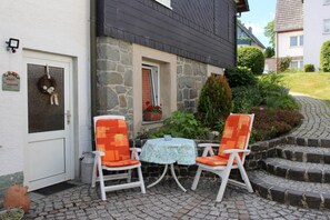Une maison en pierre avec une porte, deux chaises, une petite table et une plante en pot.