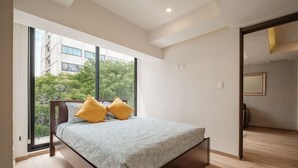 Ein modernes Schlafzimmer mit großem Fenster, einem Bett mit gemustertem Überwurf und Blick auf Grünflächen.