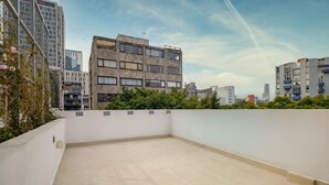 Eine Dachterrasse mit Blick auf umliegende Gebäude, einem klaren Himmel und einem Betonboden.