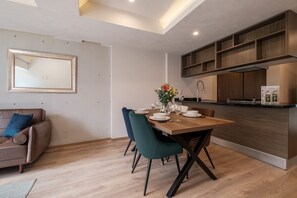 A modern kitchen with wooden cabinets, a dining table set for four, and a sofa with a blue cushion. - Brand New 2 BR Condo in Reforma - Queen Beds (Mexico City)