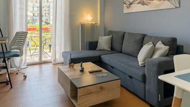 A modern living room with a grey sofa, a wooden coffee table, and a view of a balcony with outdoor furniture. - Athens City Apartment Petralona Central Gem (Athens)