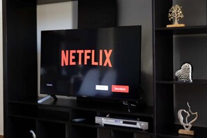 A television with the Netflix logo on the screen, placed on a black entertainment unit with shelves. - Athens City Apartment Petralona Central Gem (Athens)