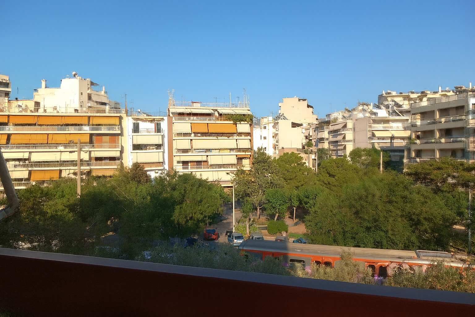 Une vue d’un quartier résidentiel avec des immeubles à plusieurs étages, des arbres et un train au premier plan.