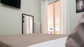 A hotel room with a bed, a television mounted on the wall, a window with curtains, and a view of the outside balcony. - Athens City Apartment Petralona Central Gem (Athens)