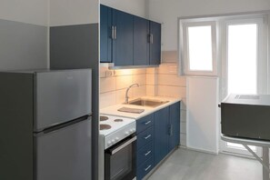 A compact kitchen with a refrigerator, stove, sink, and blue cabinets. - Athens City Apartment Petralona Central Gem (Athens)