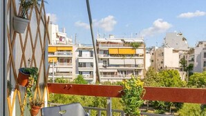 A balcony with a round table and two chairs, potted plants, and a view of residential buildings. - Athens City Apartment Petralona Central Gem (Athens)