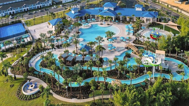 An aerial view of a resort with multiple swimming pools, a water slide, and a variety of lounge areas surrounded by palm trees. - Upstay 7BR Resort Home w Private Pool Near Disney (Davenport)
