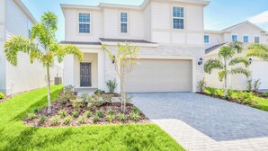 A modern two-story house with a garage, surrounded by well-maintained lawns and small trees. - Upstay 7BR Resort Home w Private Pool Near Disney (Davenport)