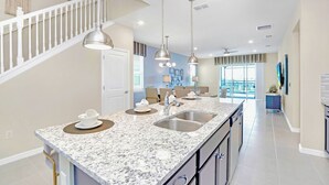 A modern kitchen with a granite countertop, stainless steel sink, and pendant lighting. - Upstay 7BR Resort Home w Private Pool Near Disney (Davenport)