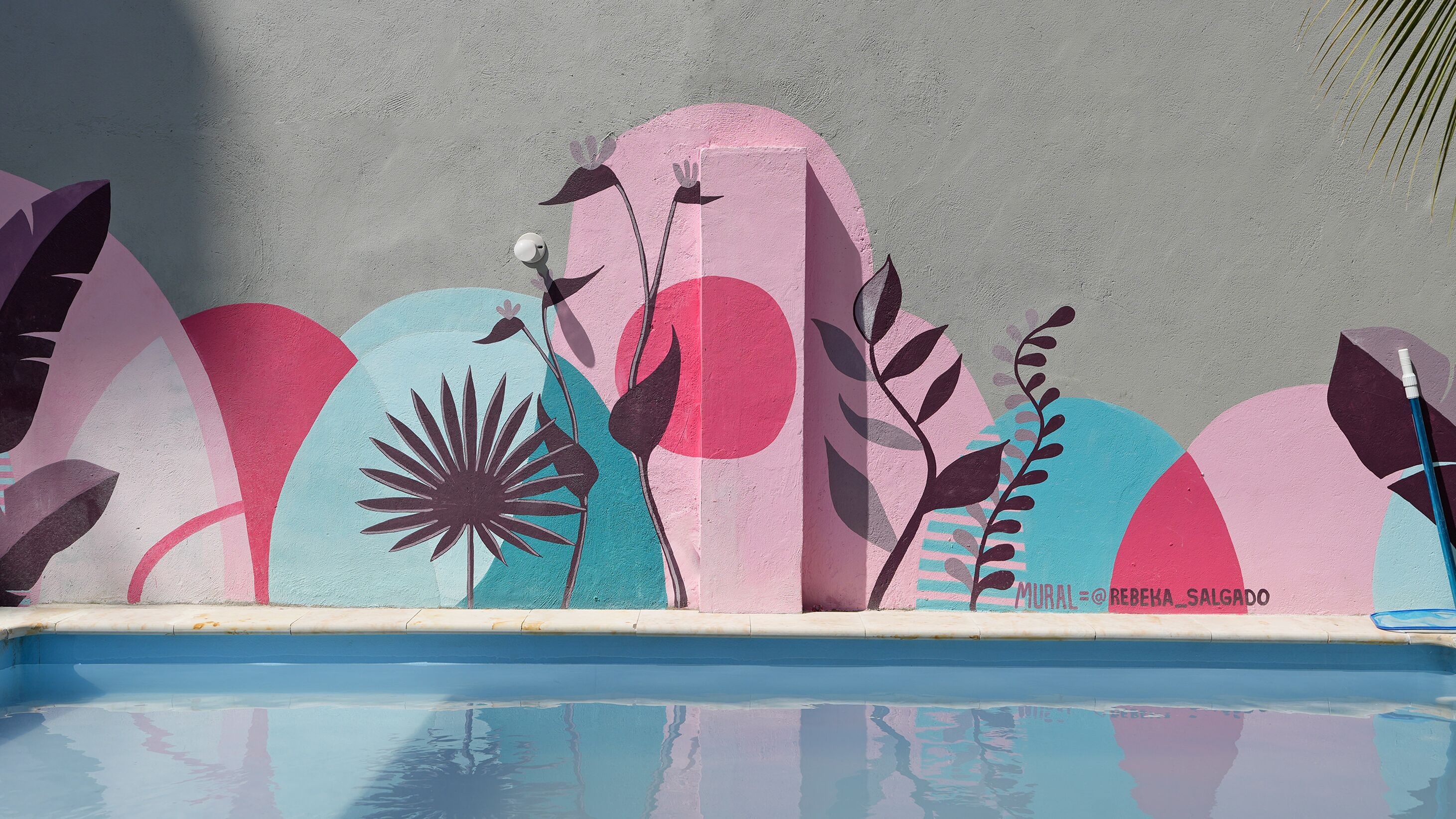Une piscine dont le mur est décoré d’une fresque colorée.