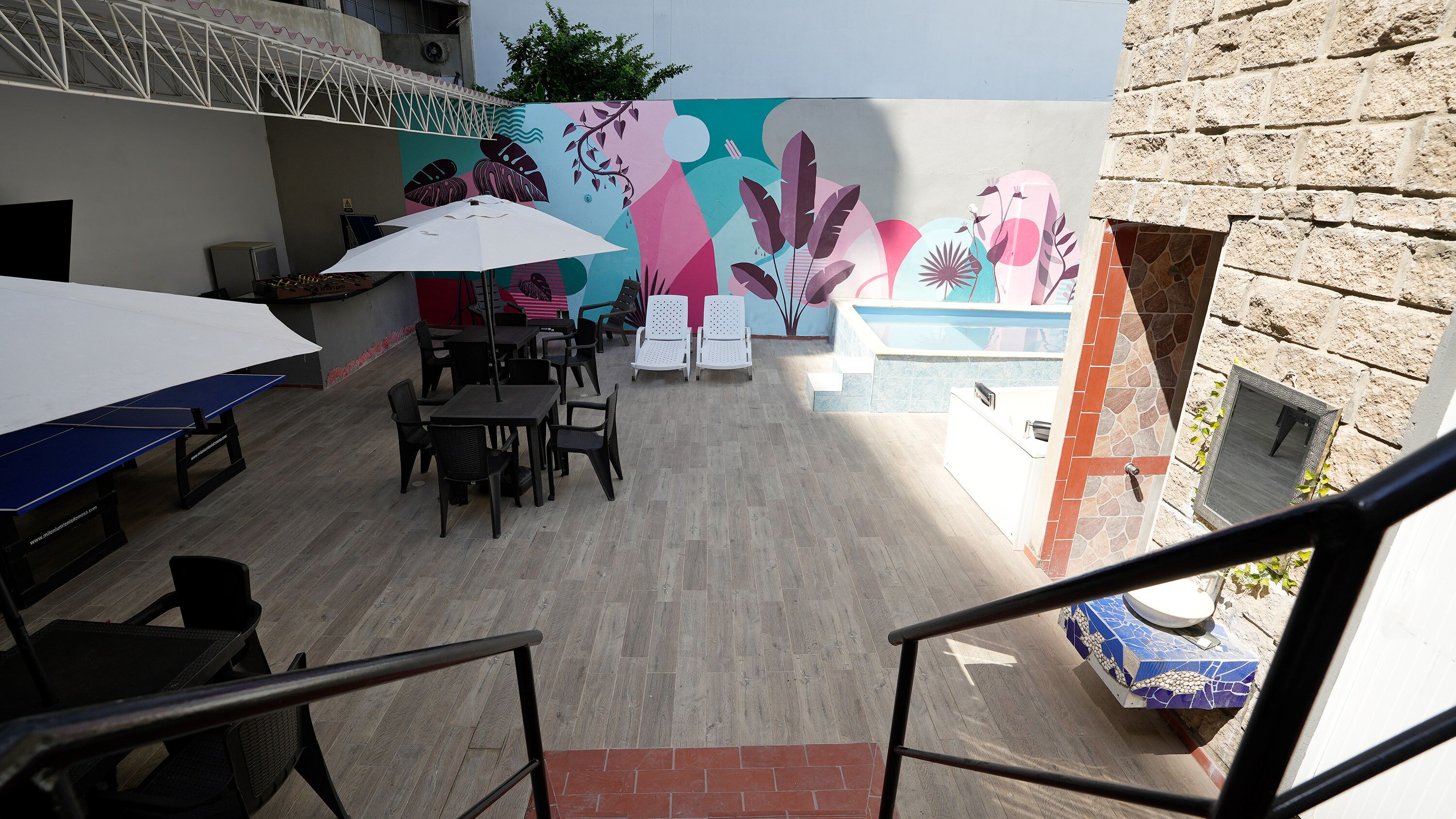 An outdoor patio area with tables and chairs, a pool, and a mural on the wall.
