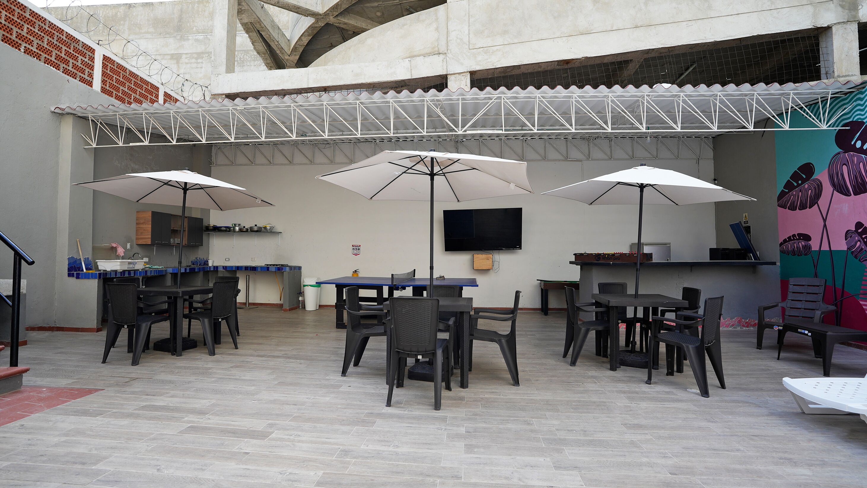 An outdoor patio area with tables and chairs, umbrellas, a bar, and a television screen.