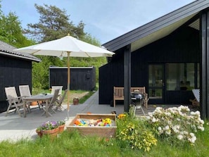 An outdoor patio with a table and chairs, a grill, and a wooden box of toys. - 5 Star Holiday Home in Hojby (Hojby)