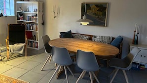 Un coin repas avec une table en bois, des chaises grises, une bibliothèque et un tableau accroché au mur.